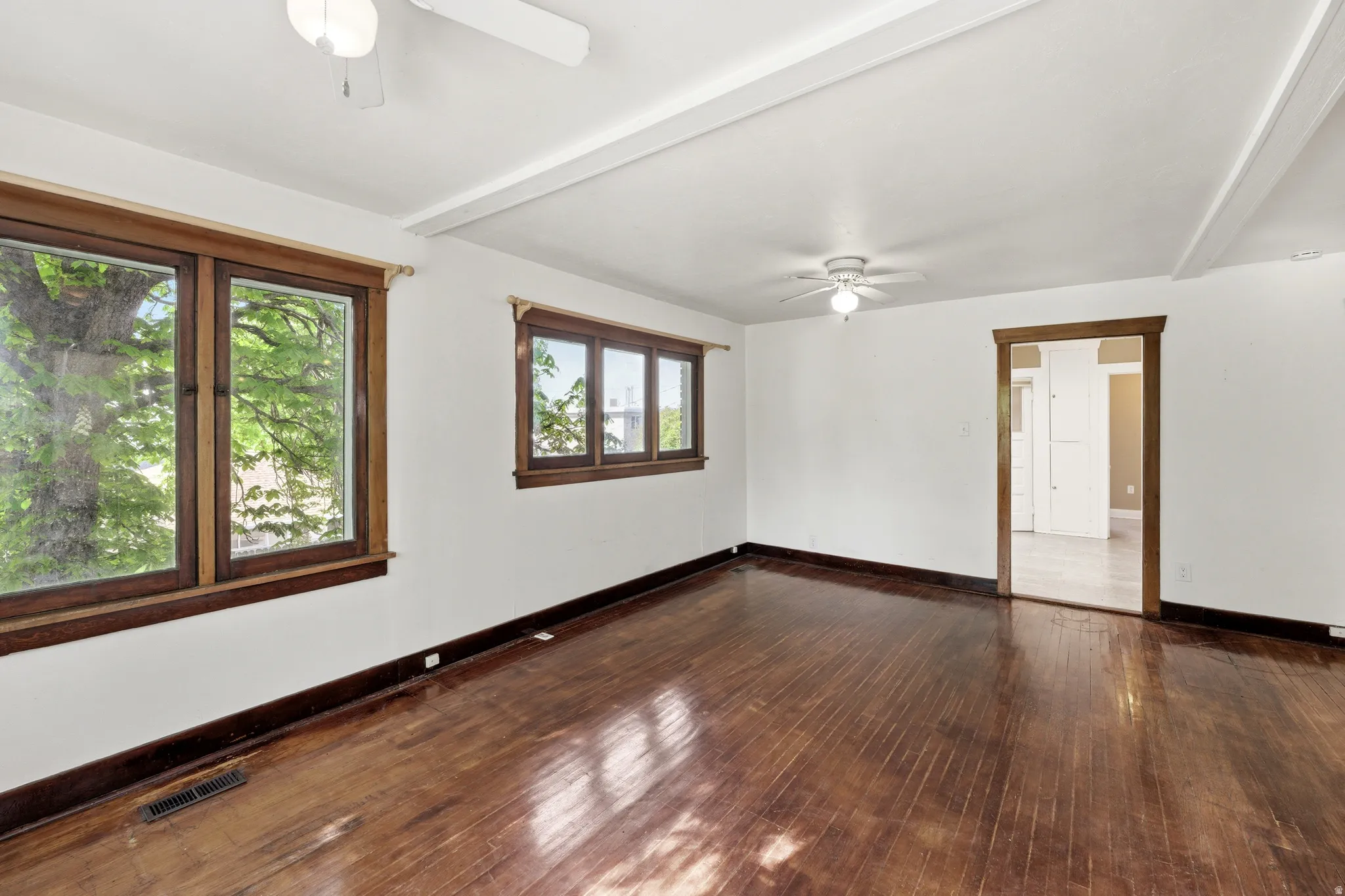 Empty room featuring a ceiling fan, beam ceiling, and dark wood-style flooring