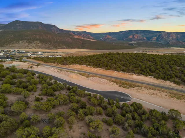 New construction road with asphalt paving, surrounded by native trees and brush, set against a mountainous backdrop