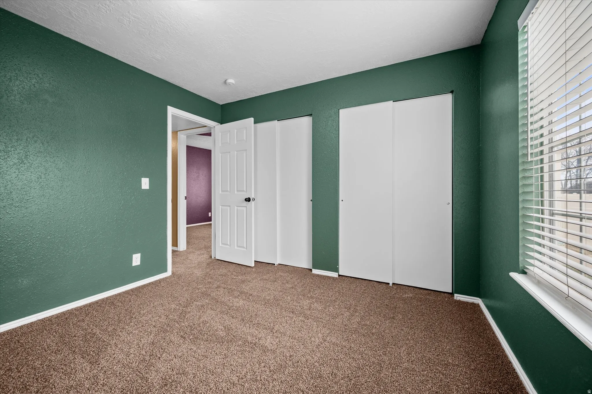 Unfurnished bedroom with two closets, carpet flooring, a textured wall, and a textured ceiling