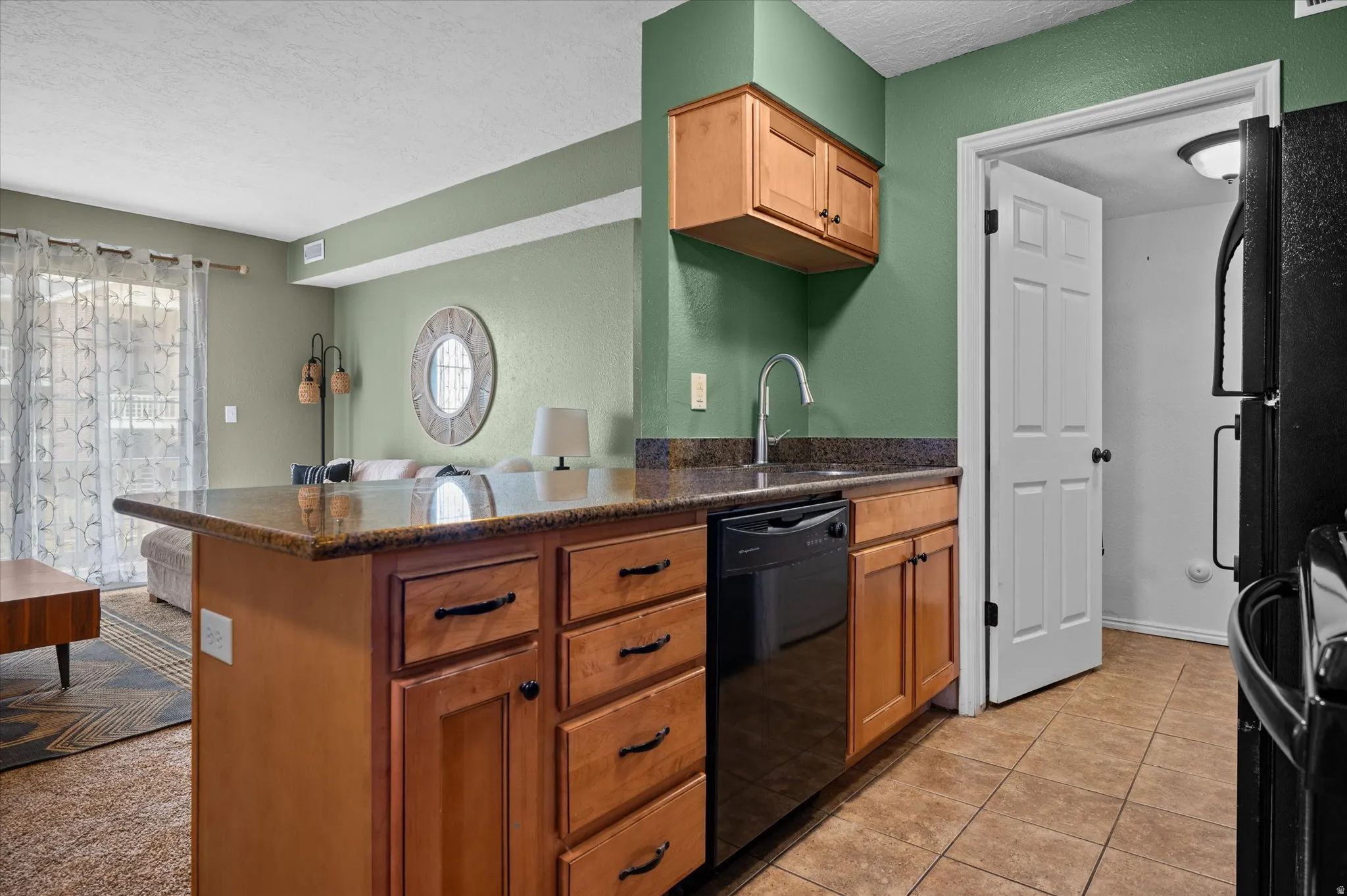 Kitchen featuring a peninsula, a textured ceiling, black appliances, dark stone countertops, and light tile patterned floors