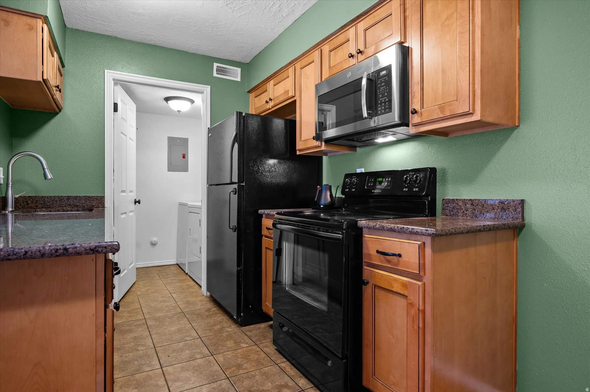 Kitchen with black appliances, dark stone countertops, a textured wall, a textured ceiling, and light tile patterned flooring