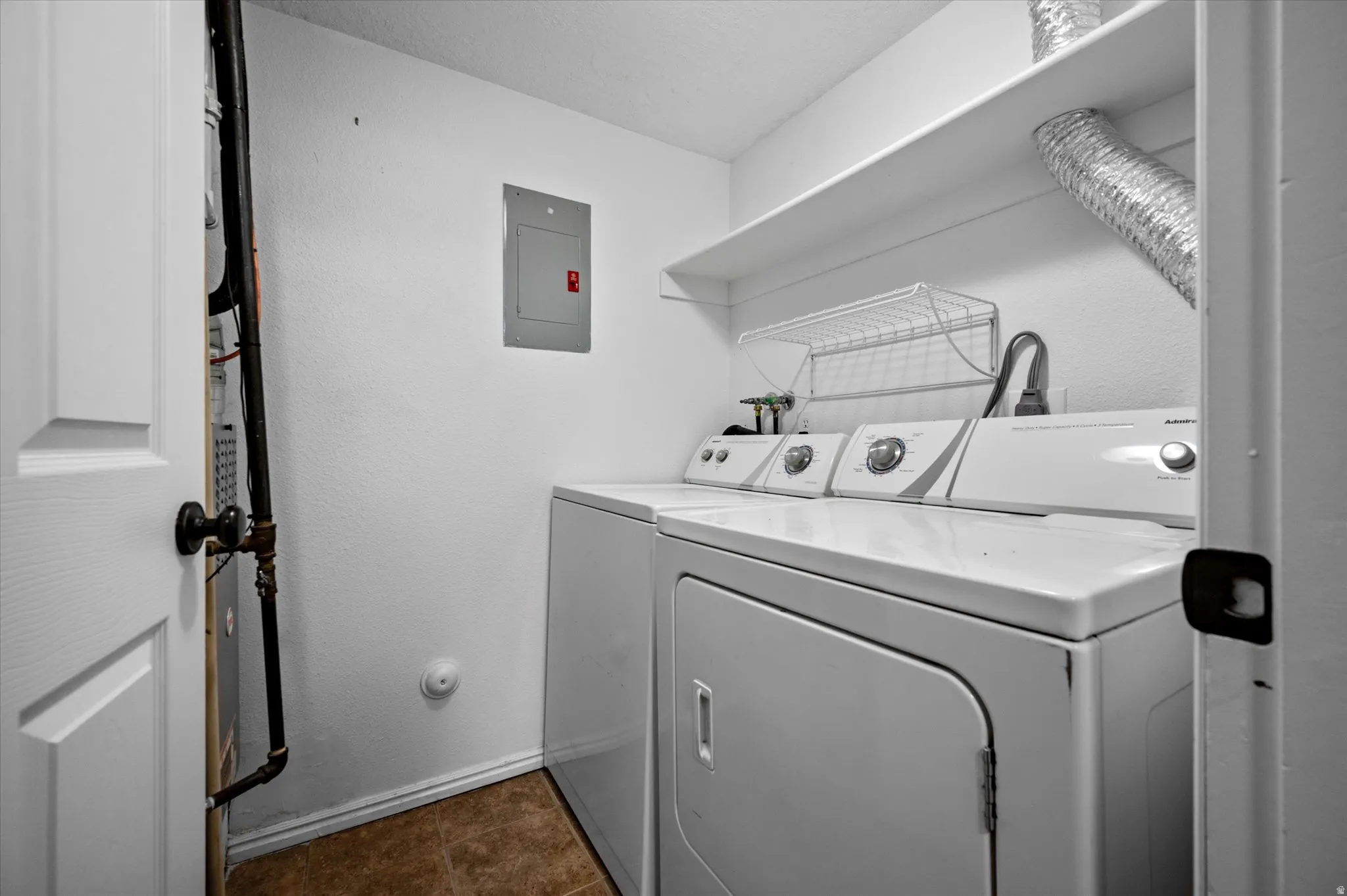 Laundry area featuring washing machine and dryer, electric panel, and a textured wall