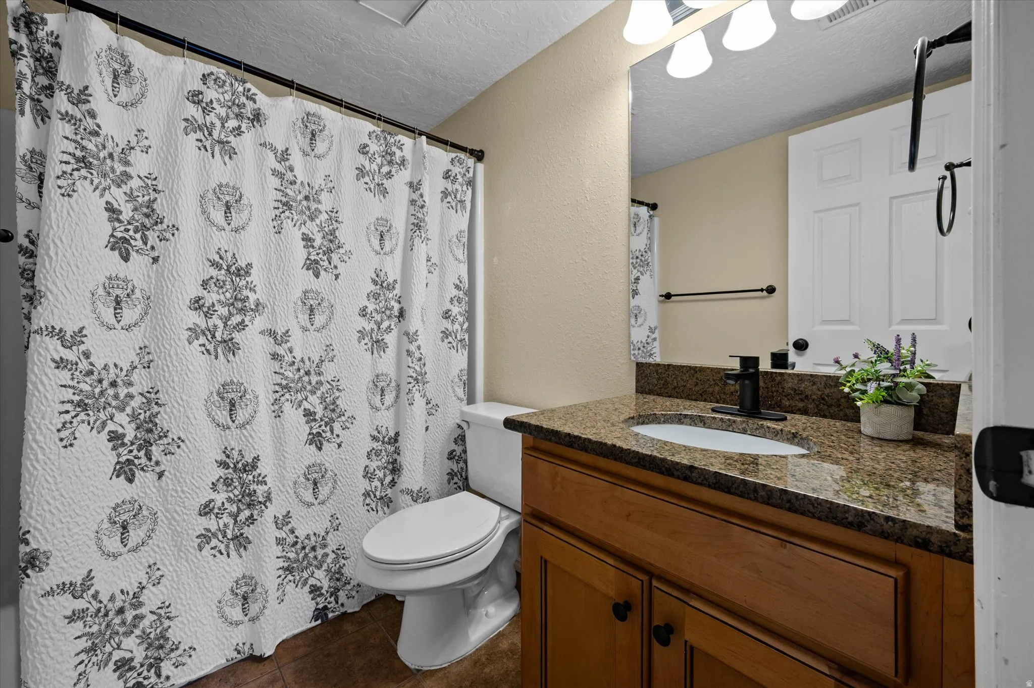 Full bath with a textured ceiling, vanity, a textured wall, curtained shower, and dark tile patterned flooring