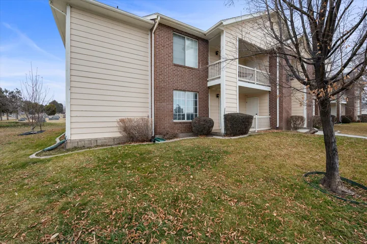 Back of house with a balcony, brick siding, and a yard