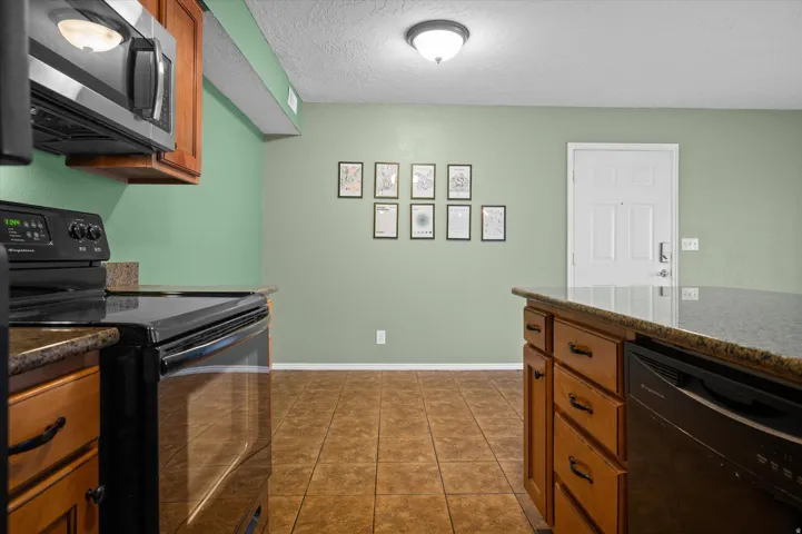 Kitchen with black appliances, a textured ceiling, wood finish cabinets, dark stone counters, and dark tile patterned floors