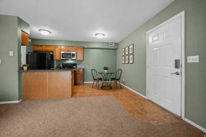 Kitchen featuring wood finish cabinetry, black appliances, light tile patterned floors, and light carpet