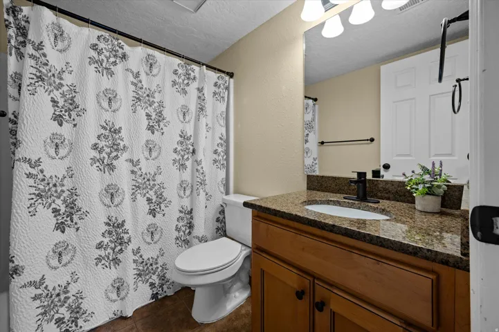 Full bath with a textured ceiling, vanity, a textured wall, curtained shower, and dark tile patterned flooring