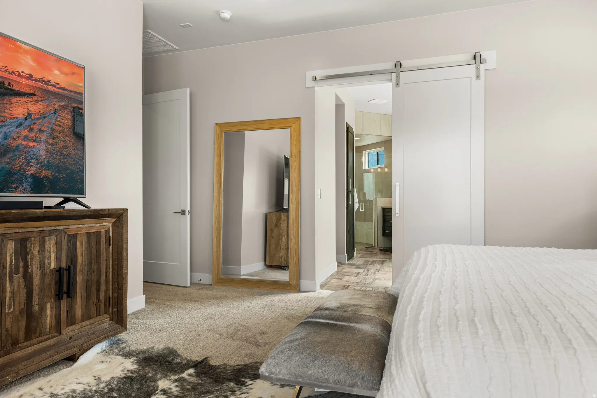 Bedroom featuring a barn door, light carpet, and ensuite bath
