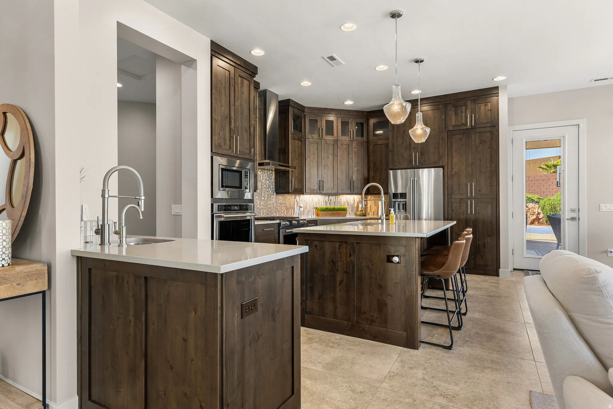 Kitchen featuring dark wood finish cabinetry, a kitchen bar, light stone counters, premium appliances, and decorative backsplash