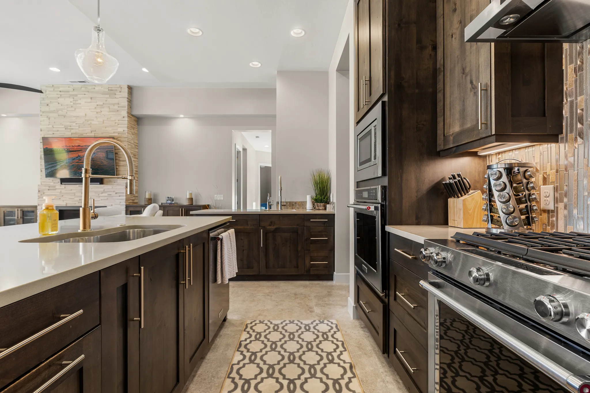 Kitchen featuring stainless steel appliances, dark wood finish cabinetry, pendant lighting, and light stone counters