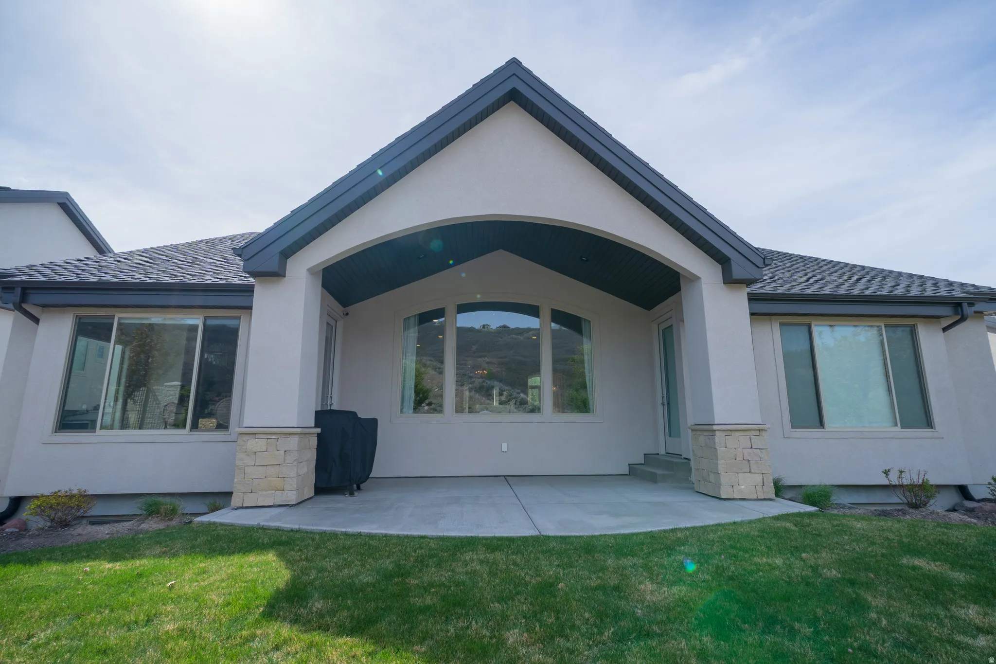 Rear view of property featuring stucco siding, a yard, a patio, and stone siding