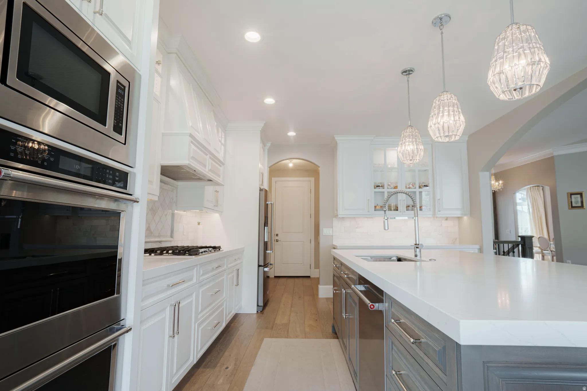 Kitchen featuring dual tone cabinets, glass insert cabinets, a chandelier, stainless steel appliances, and light wood-type flooring