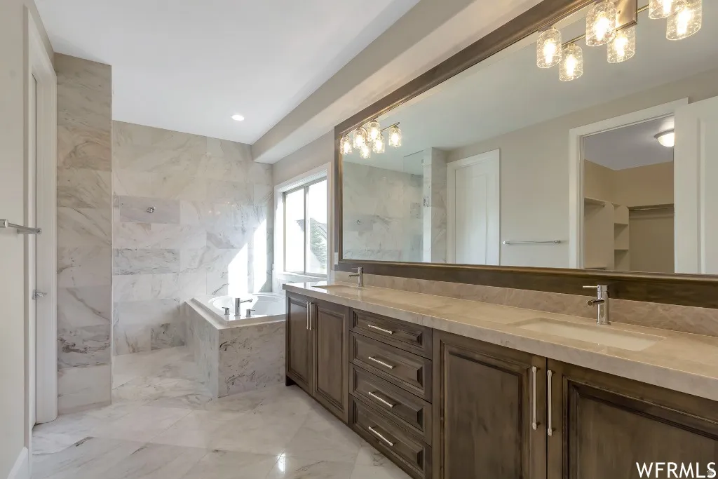 Bathroom with double vanity, a walk in closet, a garden tub, light marble finish flooring, and a marble finish shower