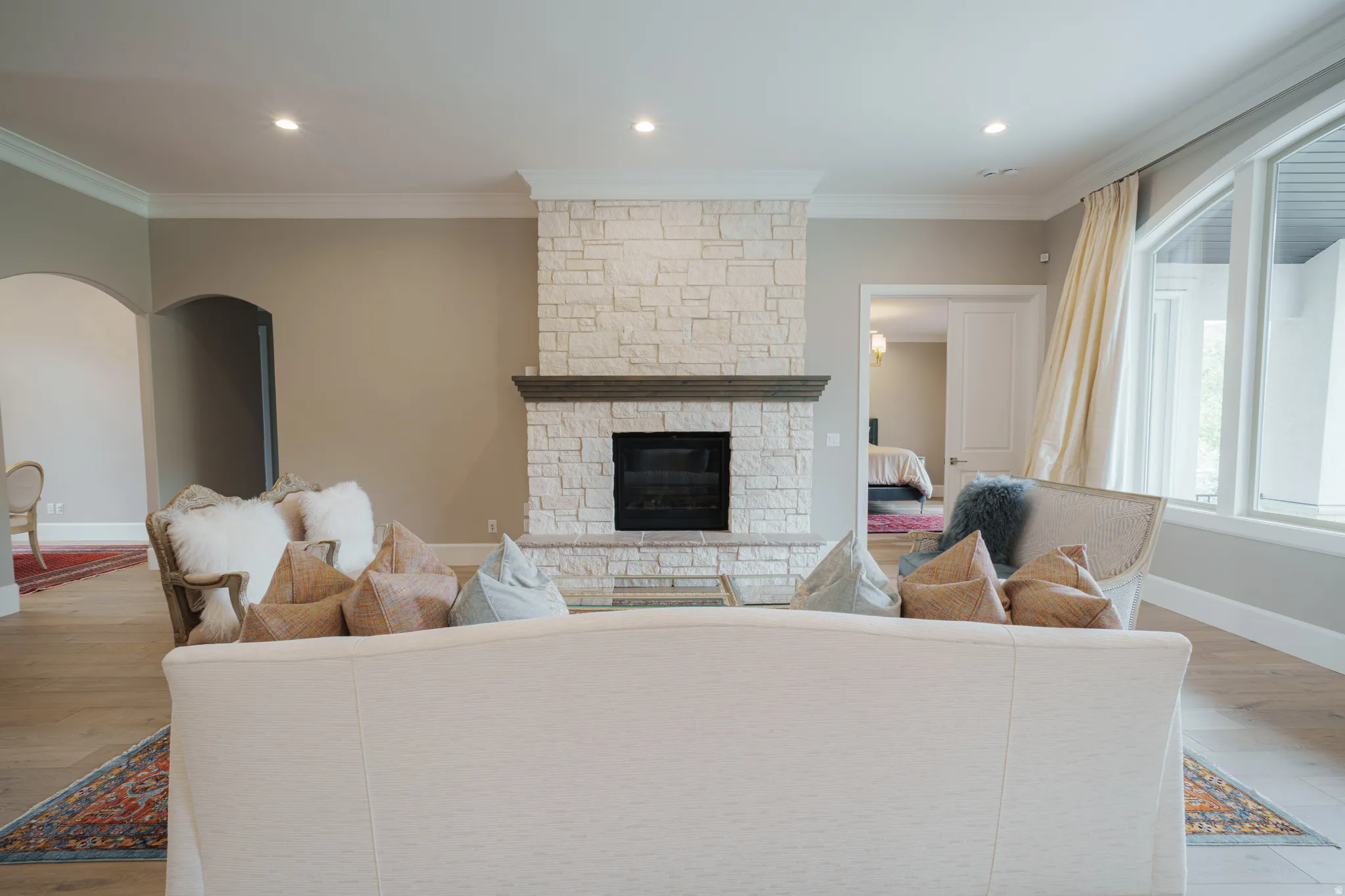 Living area with light wood-type flooring, a fireplace, crown molding, arched walkways, and recessed lighting
