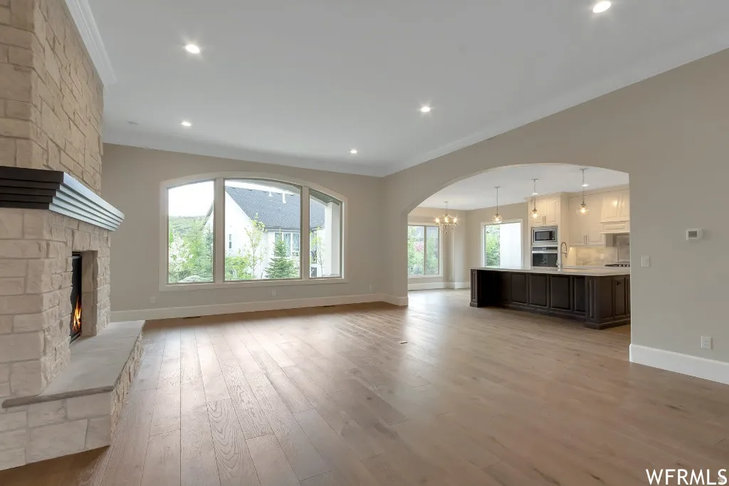 Unfurnished living room with a large fireplace, light wood-style floors, plenty of natural light, arched walkways, and crown molding