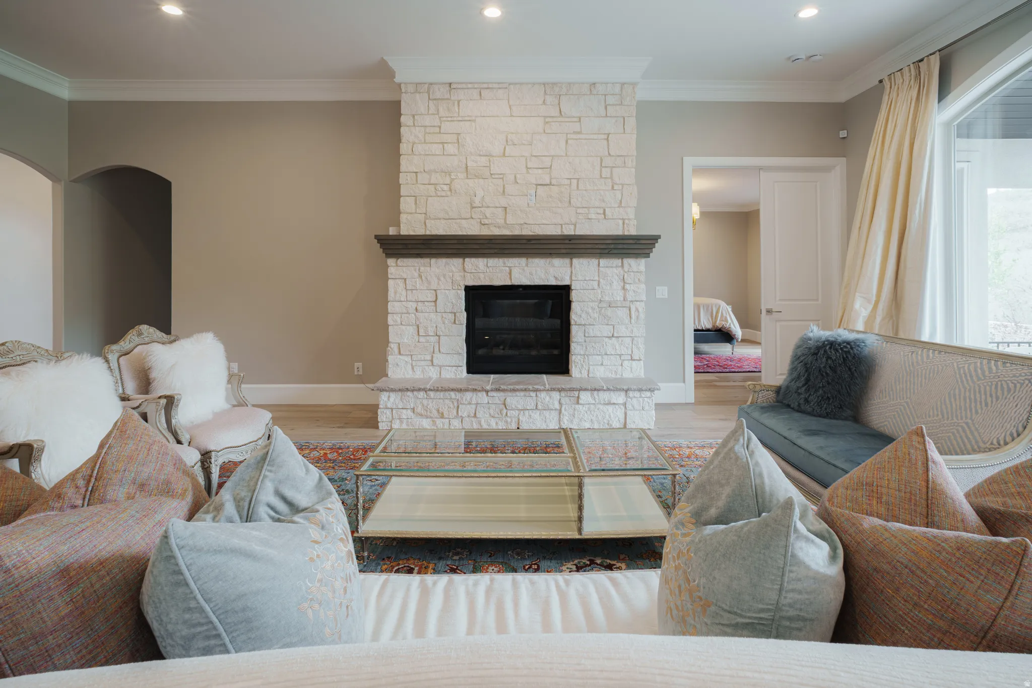 Living room with wood finished floors, a stone fireplace, ornamental molding, arched walkways, and recessed lighting