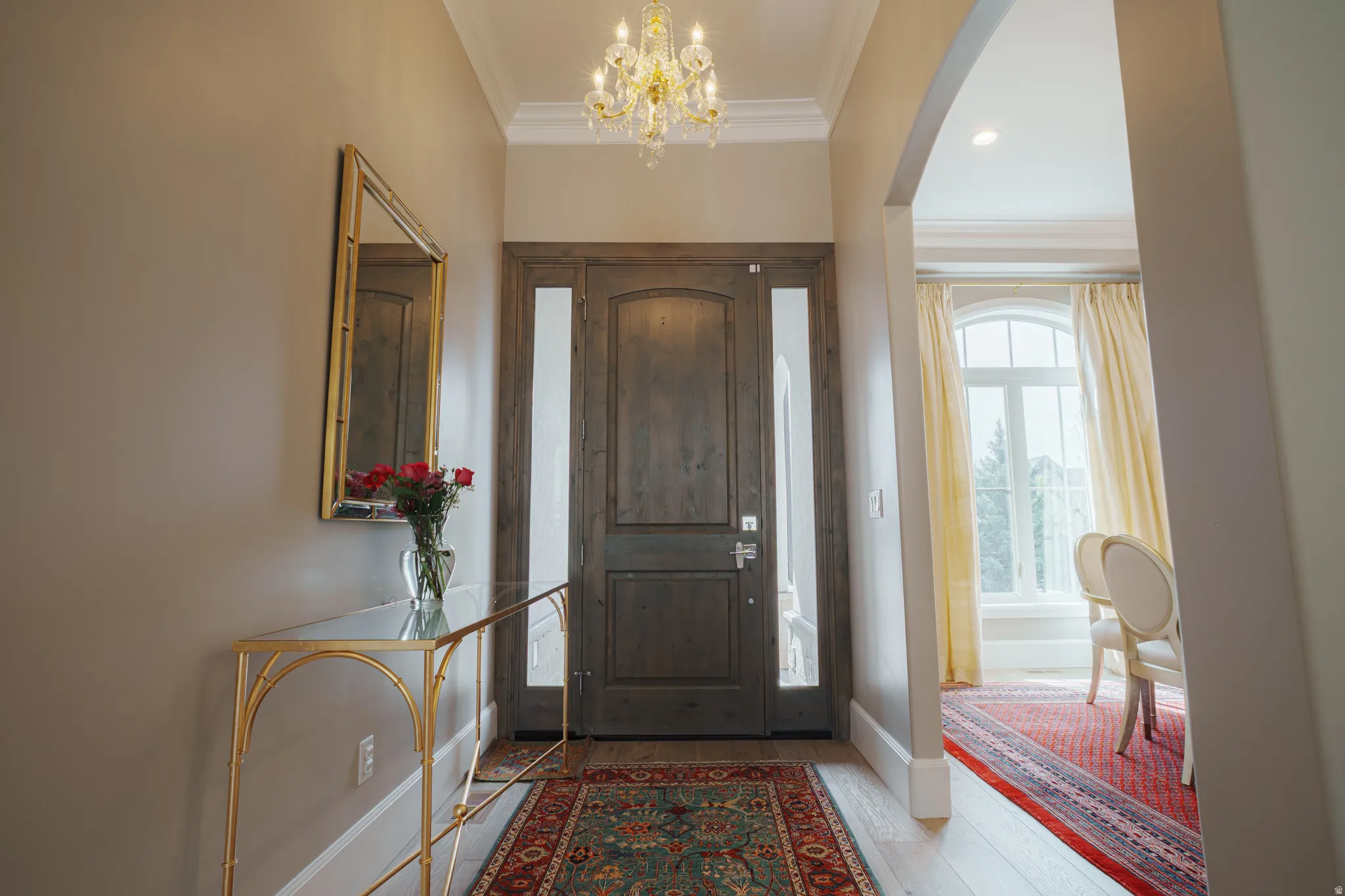 Foyer entrance with crown molding, suspended lighting, light wood-style flooring, and arched walkways