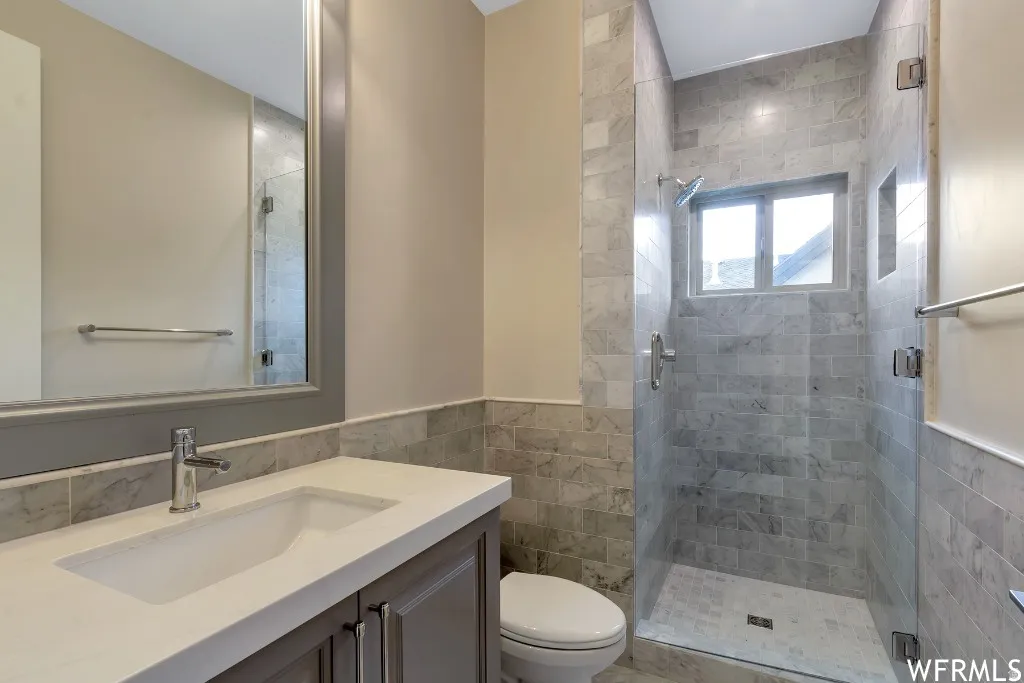 Bathroom with tile walls, vanity, a stall shower, and a wainscoted wall