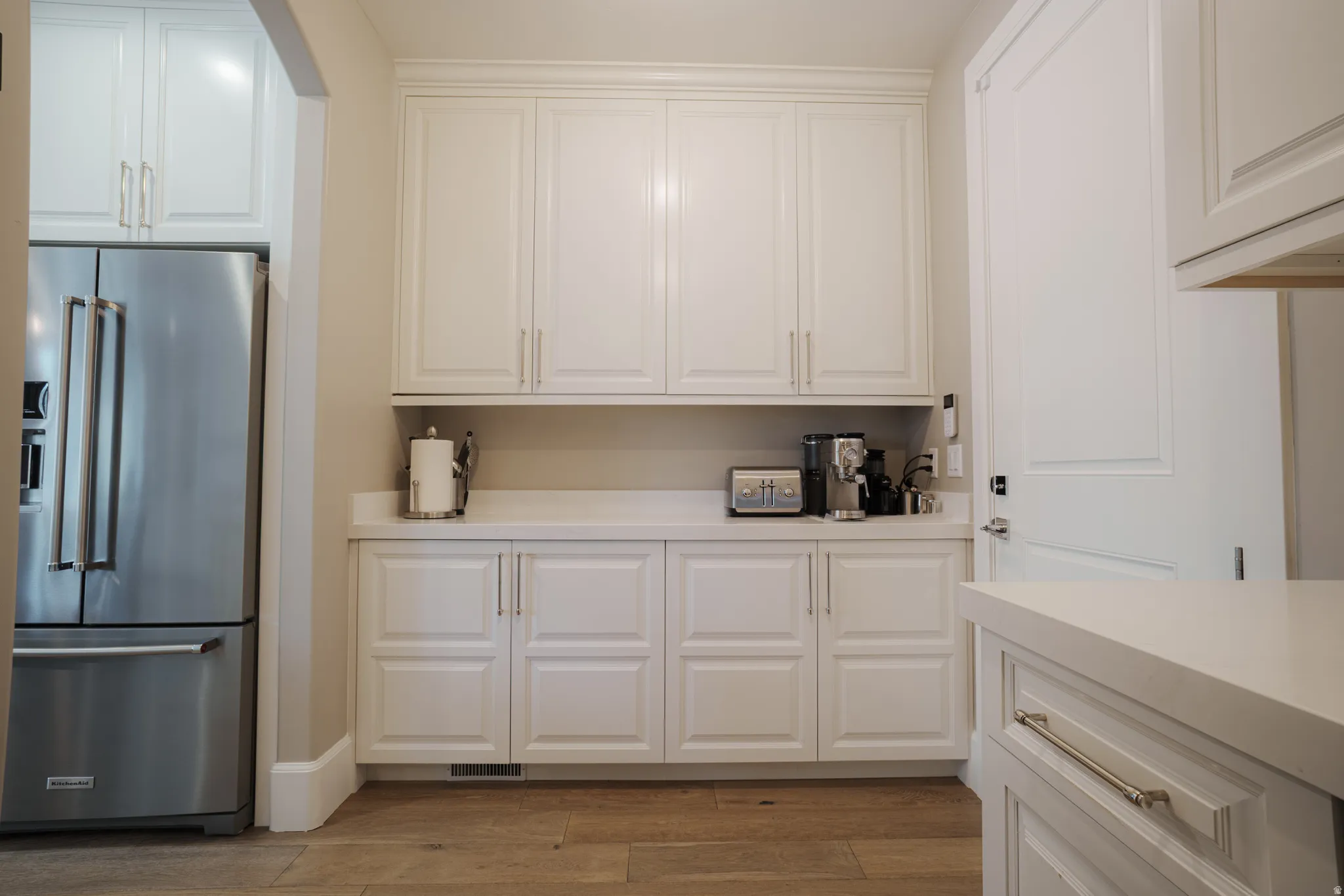 Kitchen with high end fridge, white cabinets, light wood-style floors, and light stone counters