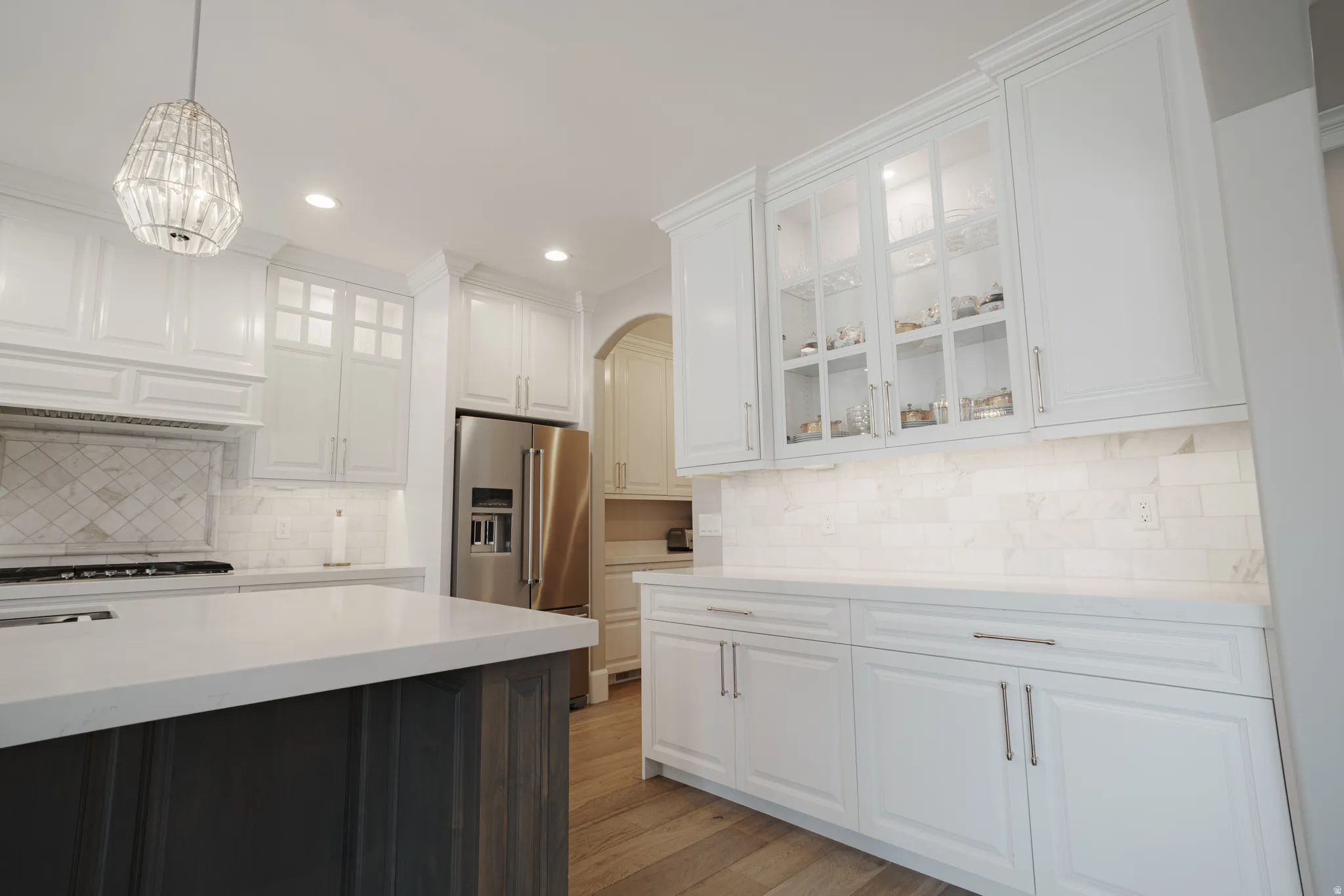 Kitchen with glass fronted cabinets, arched walkways, light stone countertops, light wood-style flooring, and two tone cabinets