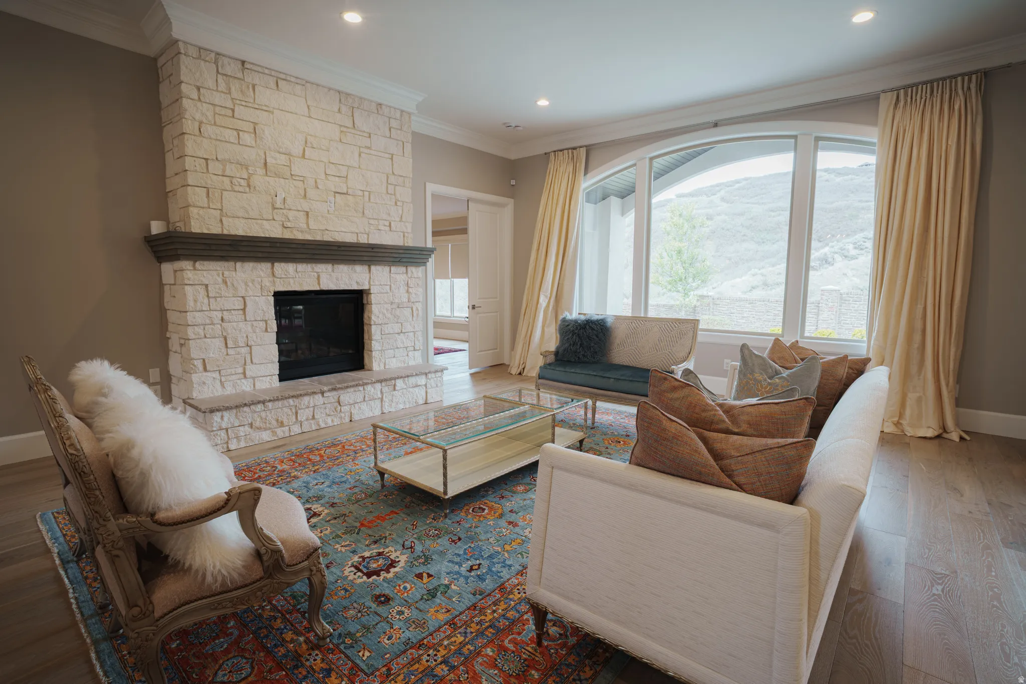 Living room featuring wood-type flooring, ornamental molding, a stone fireplace, and recessed lighting