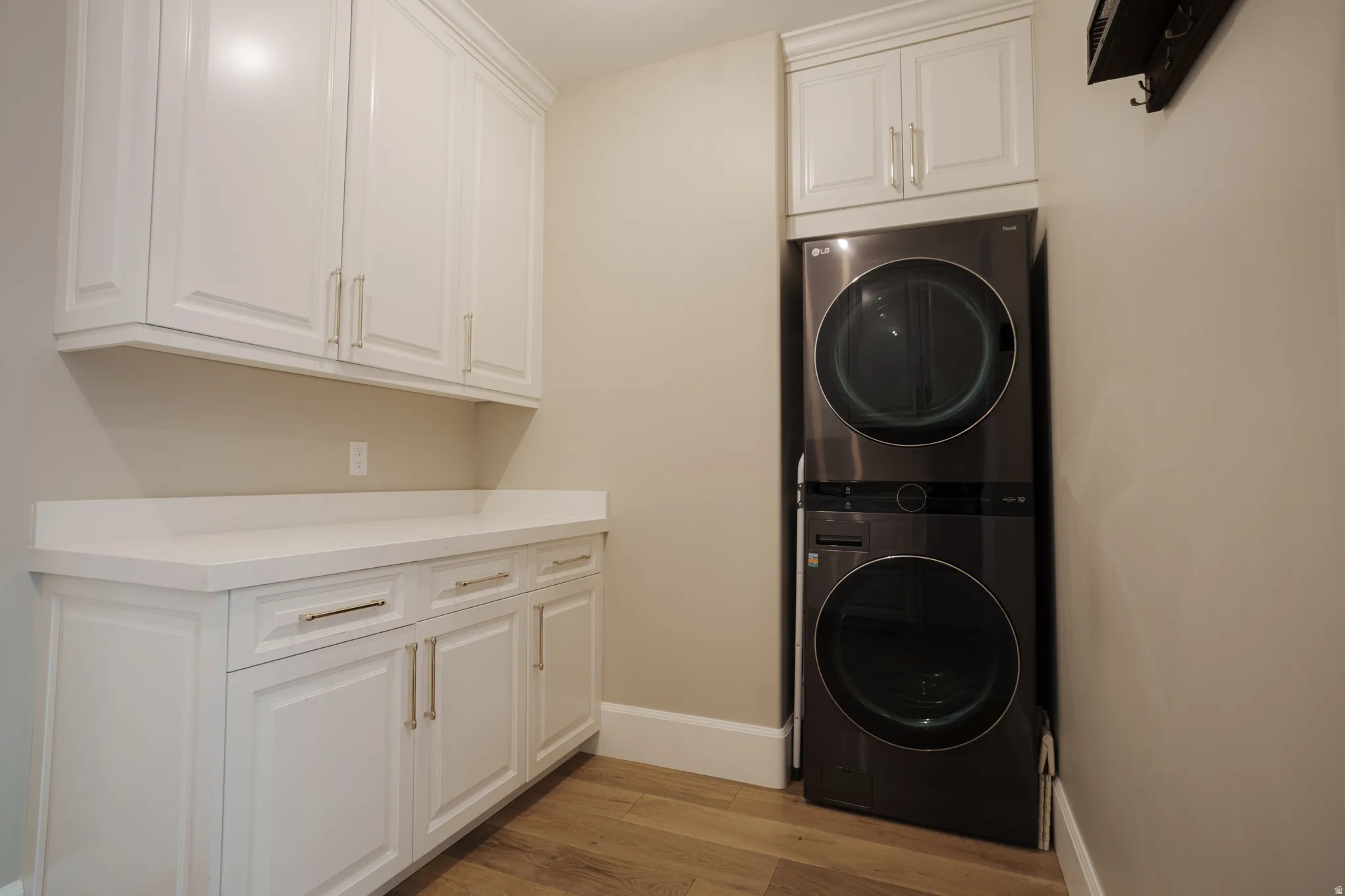 Laundry area featuring light wood-type flooring, stacked washing machine and dryer, and cabinet space