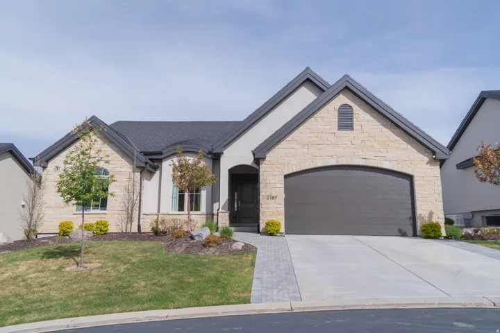 French provincial home with stone siding, concrete driveway, an attached garage, a front lawn, and stucco siding