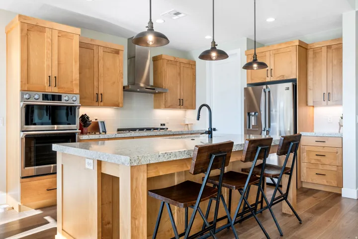 Kitchen featuring hanging light fixtures, a center island with sink, stainless steel appliances, dark wood-style floors, and decorative backsplash