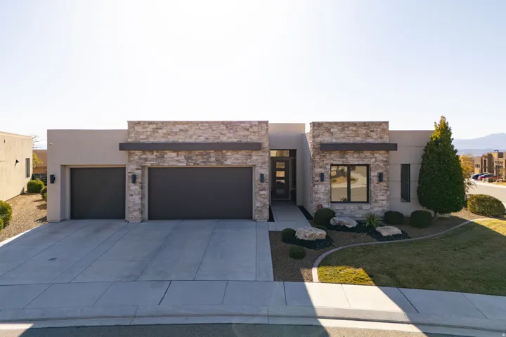 Modern home featuring an attached garage, driveway, a front lawn, stucco siding, and stone siding