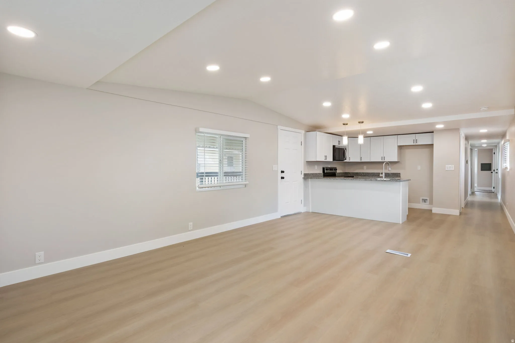 Kitchen featuring open floor plan, light wood-type flooring, vaulted ceiling, recessed lighting, and white cabinets