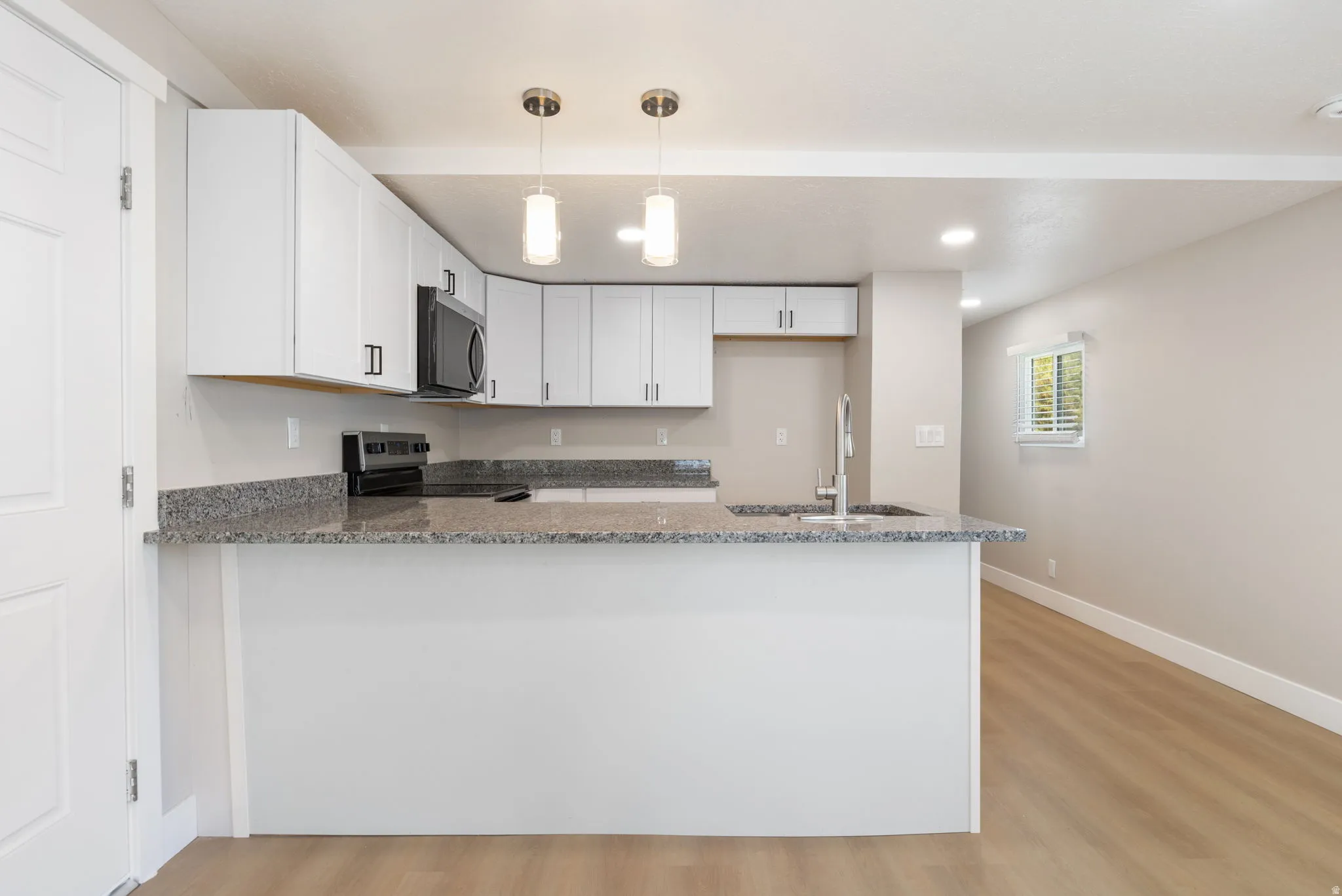 Kitchen with a peninsula, dark stone countertops, white cabinets, and light wood-style flooring