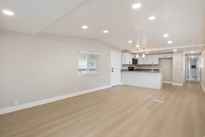 Kitchen featuring open floor plan, light wood-type flooring, vaulted ceiling, recessed lighting, and white cabinets