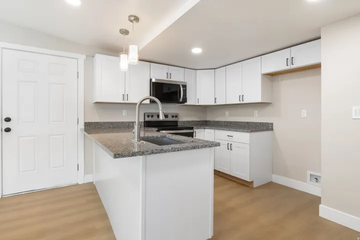 Kitchen featuring white cabinetry, a peninsula, light wood-style floors, dark stone counters, and stainless steel appliances