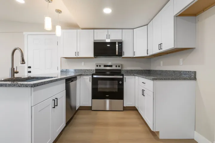 Kitchen featuring stainless steel appliances, dark stone countertops, white cabinetry, a peninsula, and hanging light fixtures
