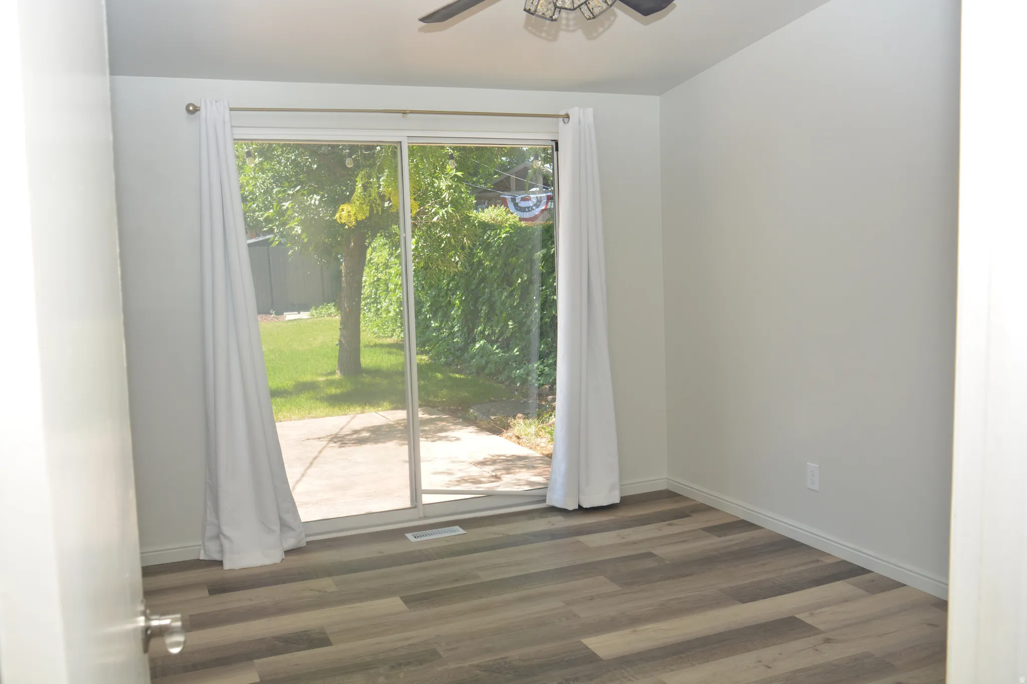 Sliding glass door leading to outdoor patio, complemented by wood-finish flooring and a ceiling fan