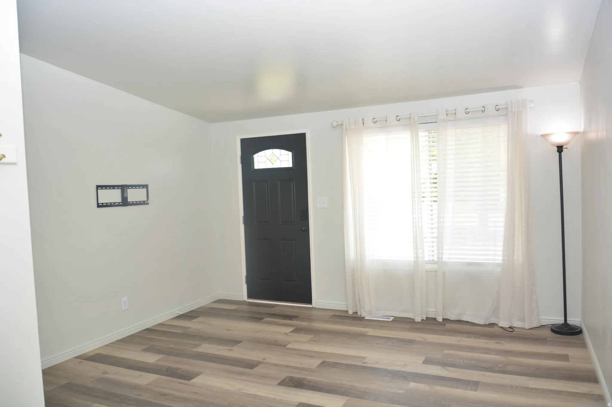 Entryway featuring wood-finish flooring, a dark-paneled door with an arched glass insert, and a double window with blinds