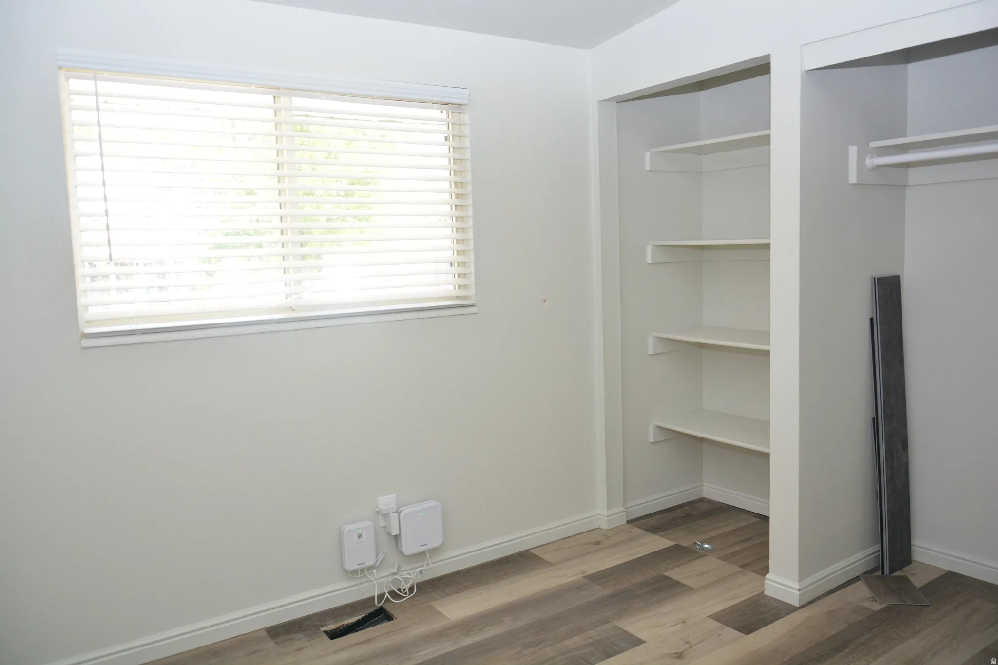 Room featuring wood-finish flooring, a window with horizontal blinds, and a built-in closet with shelving and hanging rods