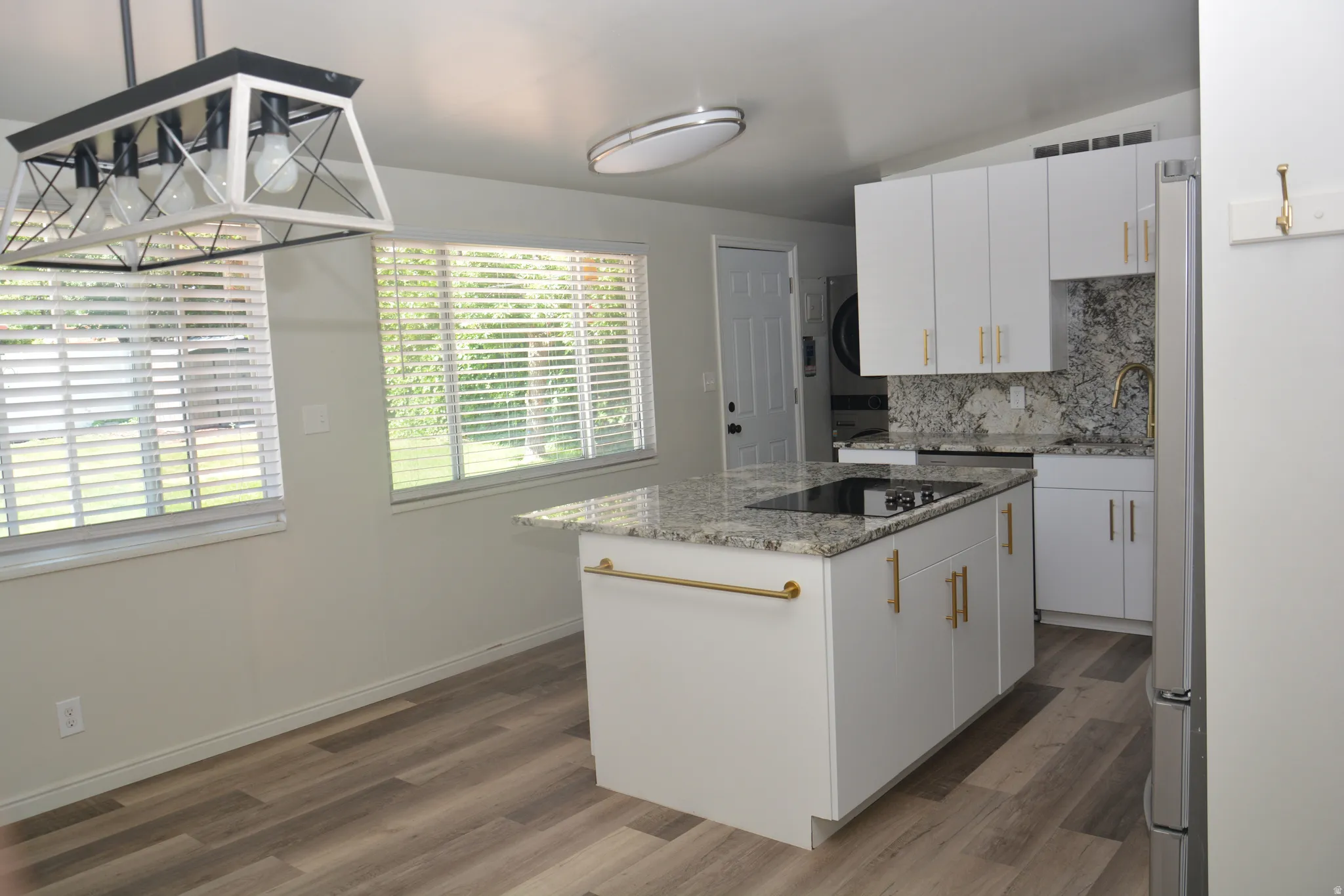 Kitchen featuring a granite-topped island with an integrated cooktop, white cabinetry, and gold-tone hardware