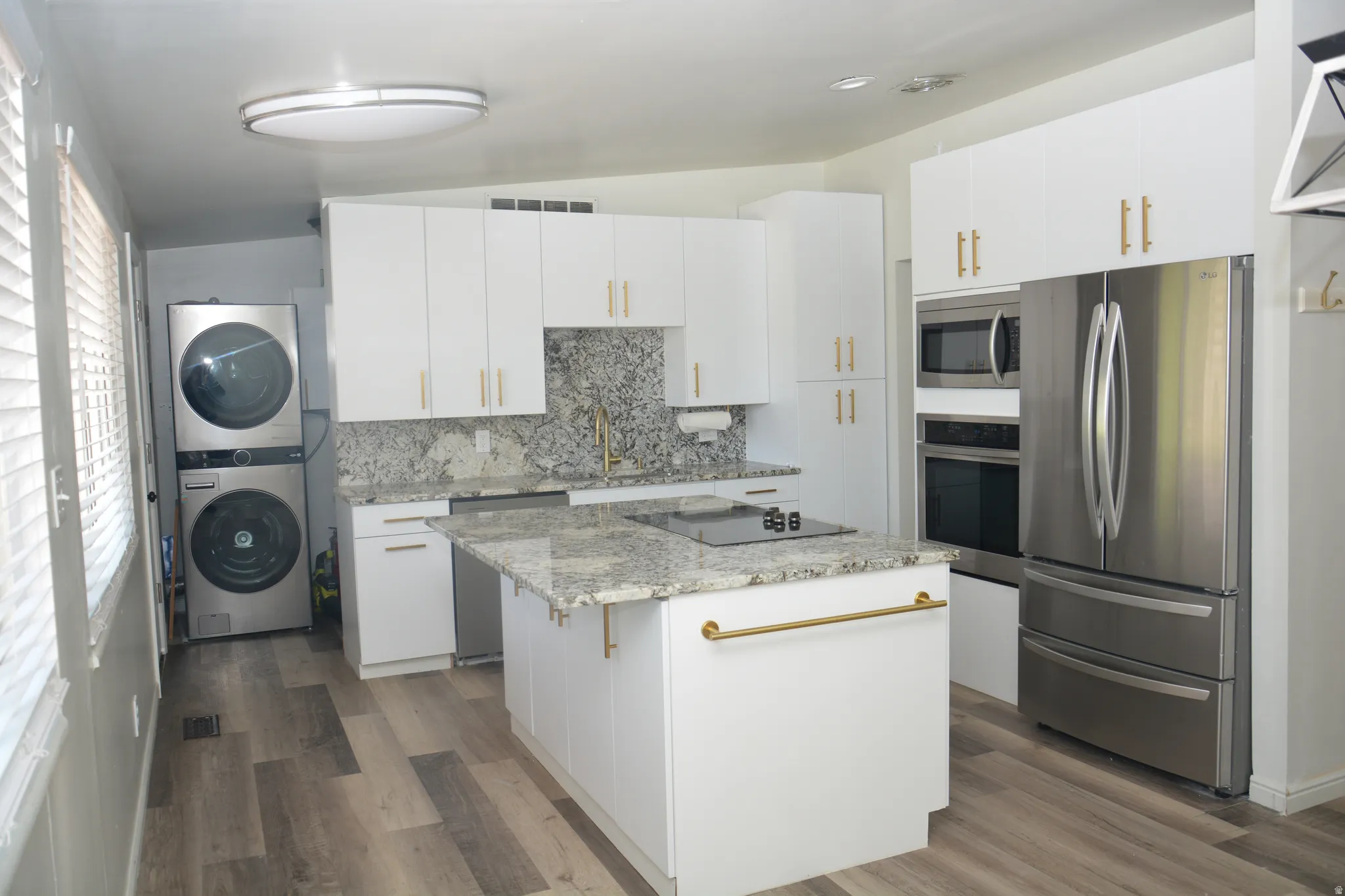 Modern kitchen featuring white cabinetry with gold-tone hardware, granite countertops, stainless steel appliances, and wood-finish flooring