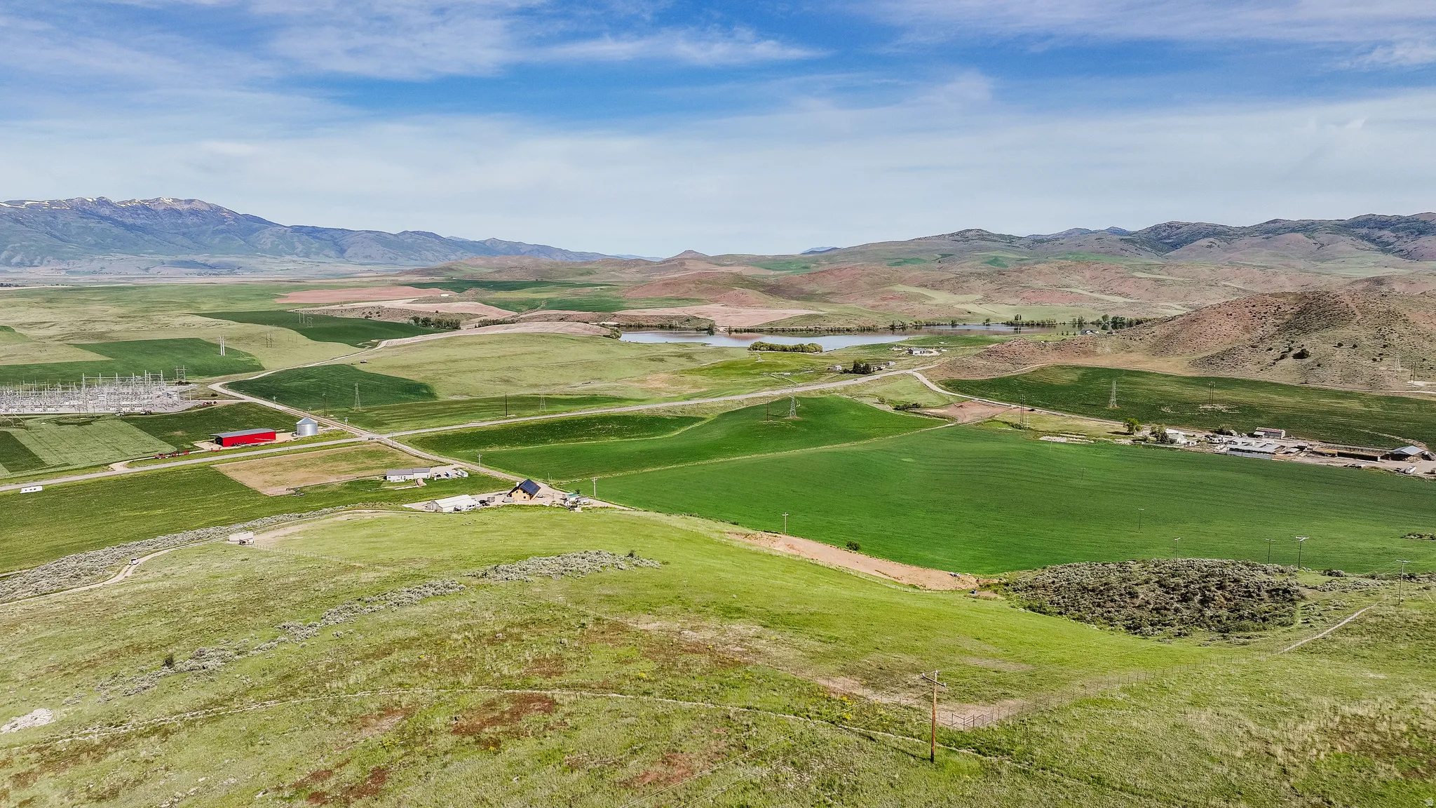 Expansive rural landscape featuring rolling green hills, a distant mountain range, and scattered agricultural fields