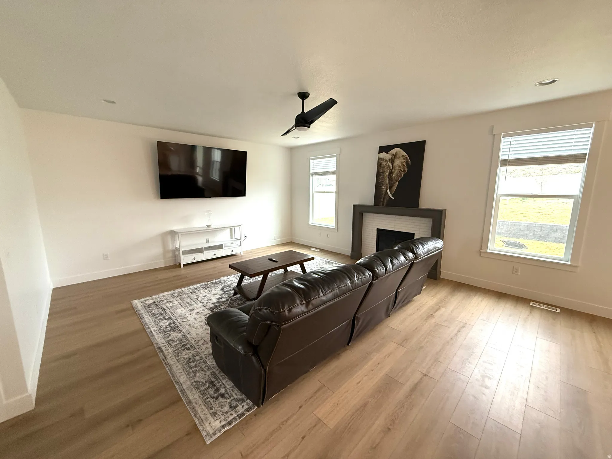 Living area with light wood-style floors, ceiling fan, and a brick fireplace