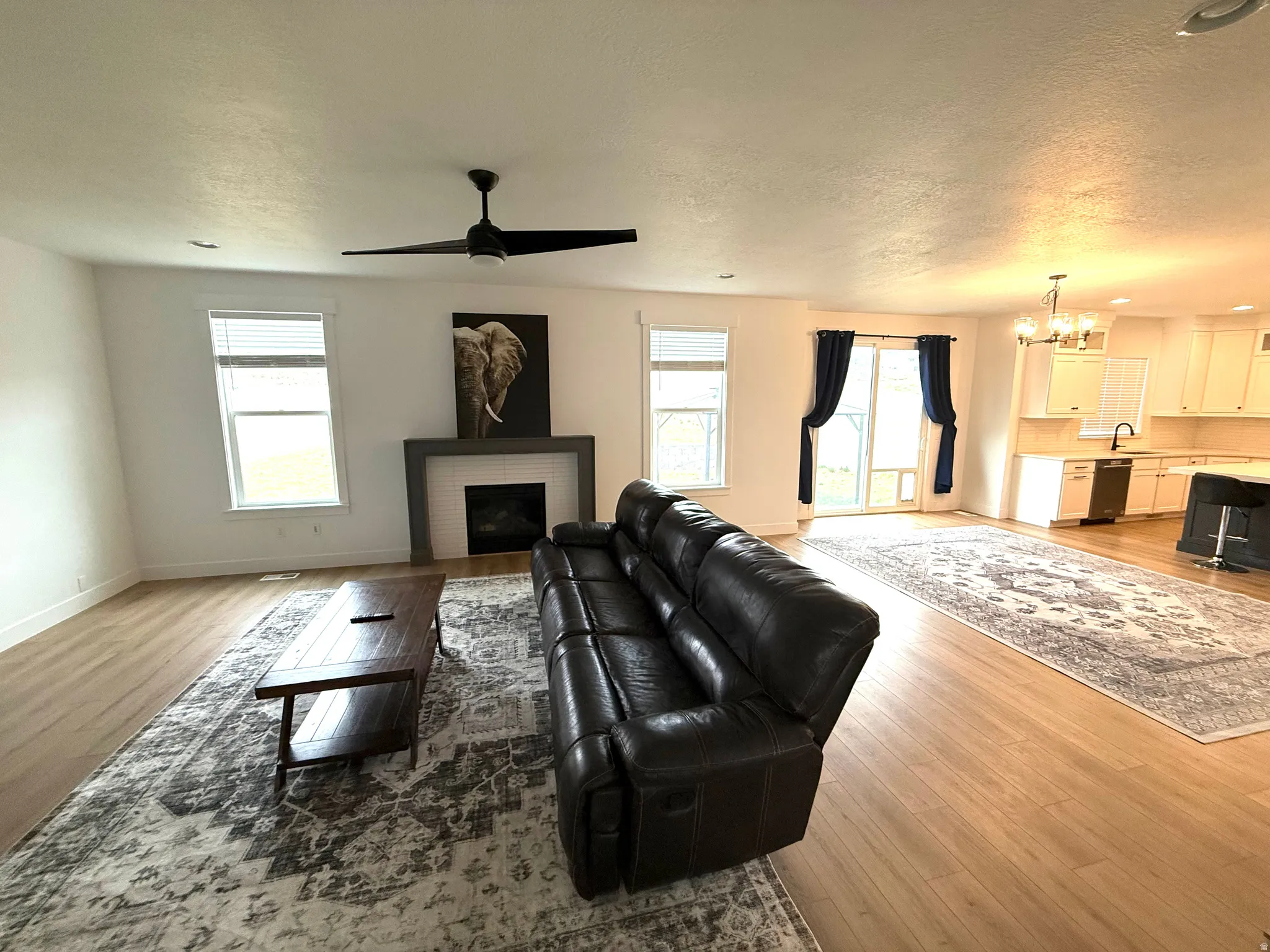 Living room with suspended lighting, a fireplace, a textured ceiling, healthy amount of natural light, and light wood-type flooring