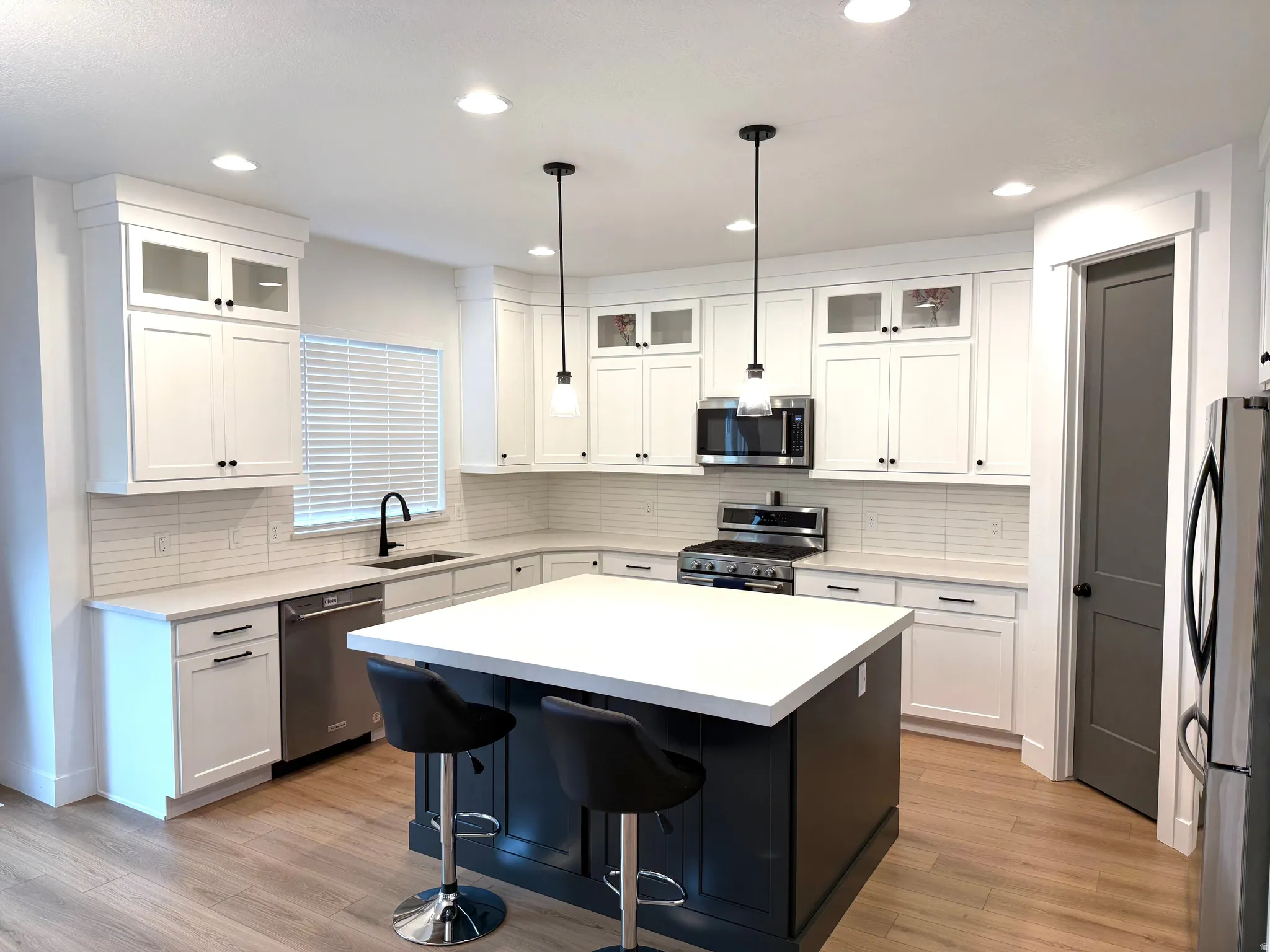Kitchen featuring glass fronted cabinets, stainless steel appliances, a kitchen breakfast bar, decorative light fixtures, and white cabinets