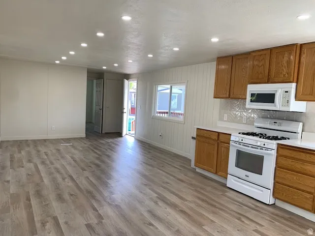 Kitchen featuring light countertops, white appliances, wood finish cabinets, recessed lighting, and light wood-type flooring