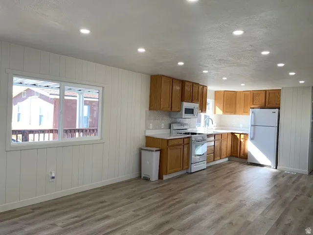 Kitchen with light countertops, wooden walls, white appliances, wood finish cabinets, and light wood-style floors