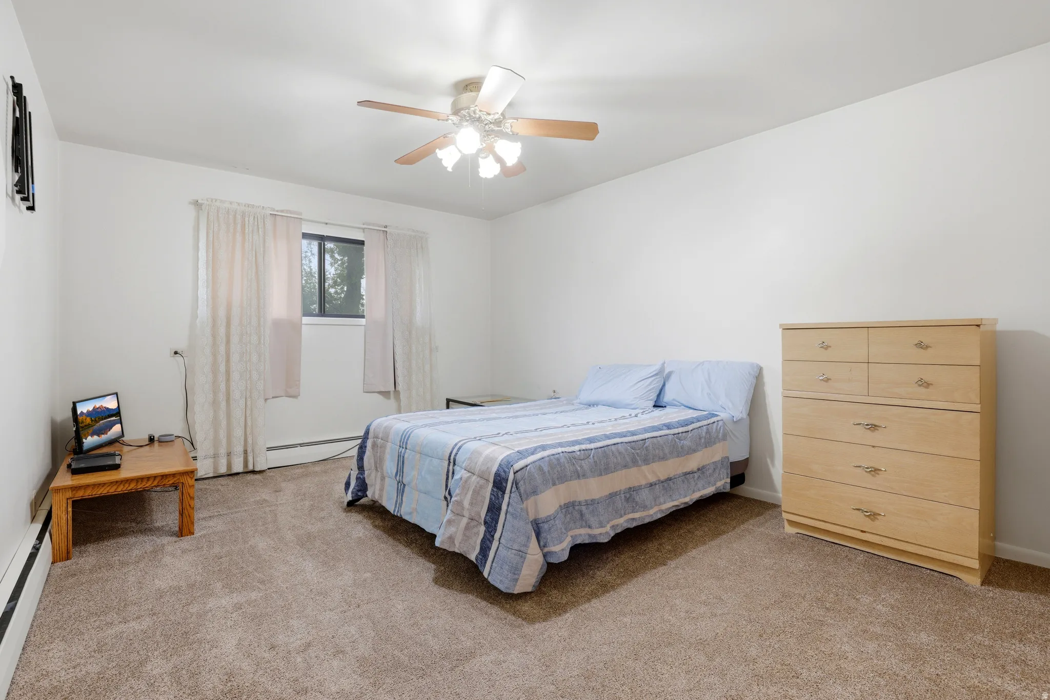 Bedroom with light carpet, ceiling fan, and a baseboard heating unit