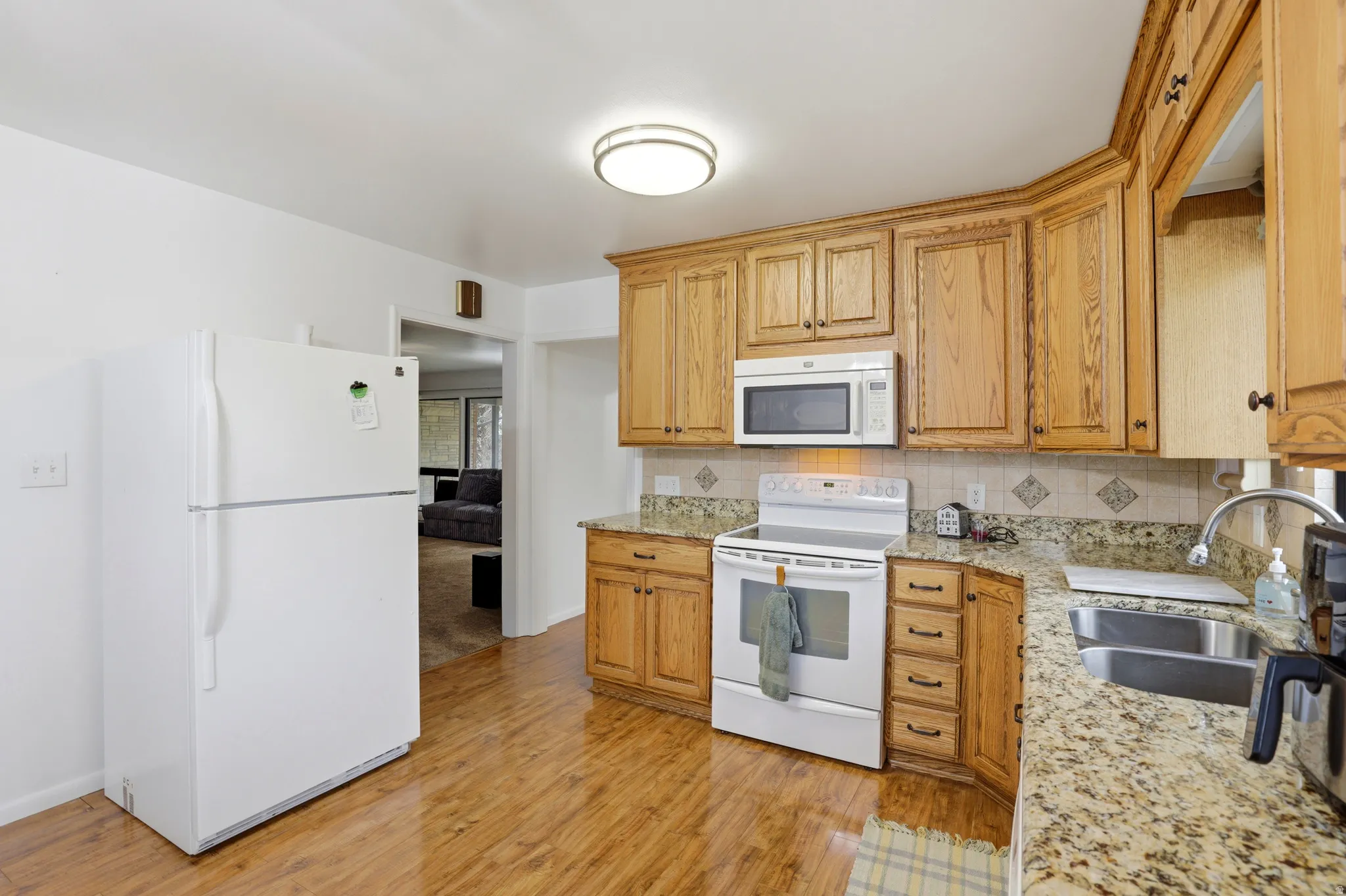 Kitchen with white appliances, tasteful backsplash, light stone counters, and light wood finished floors