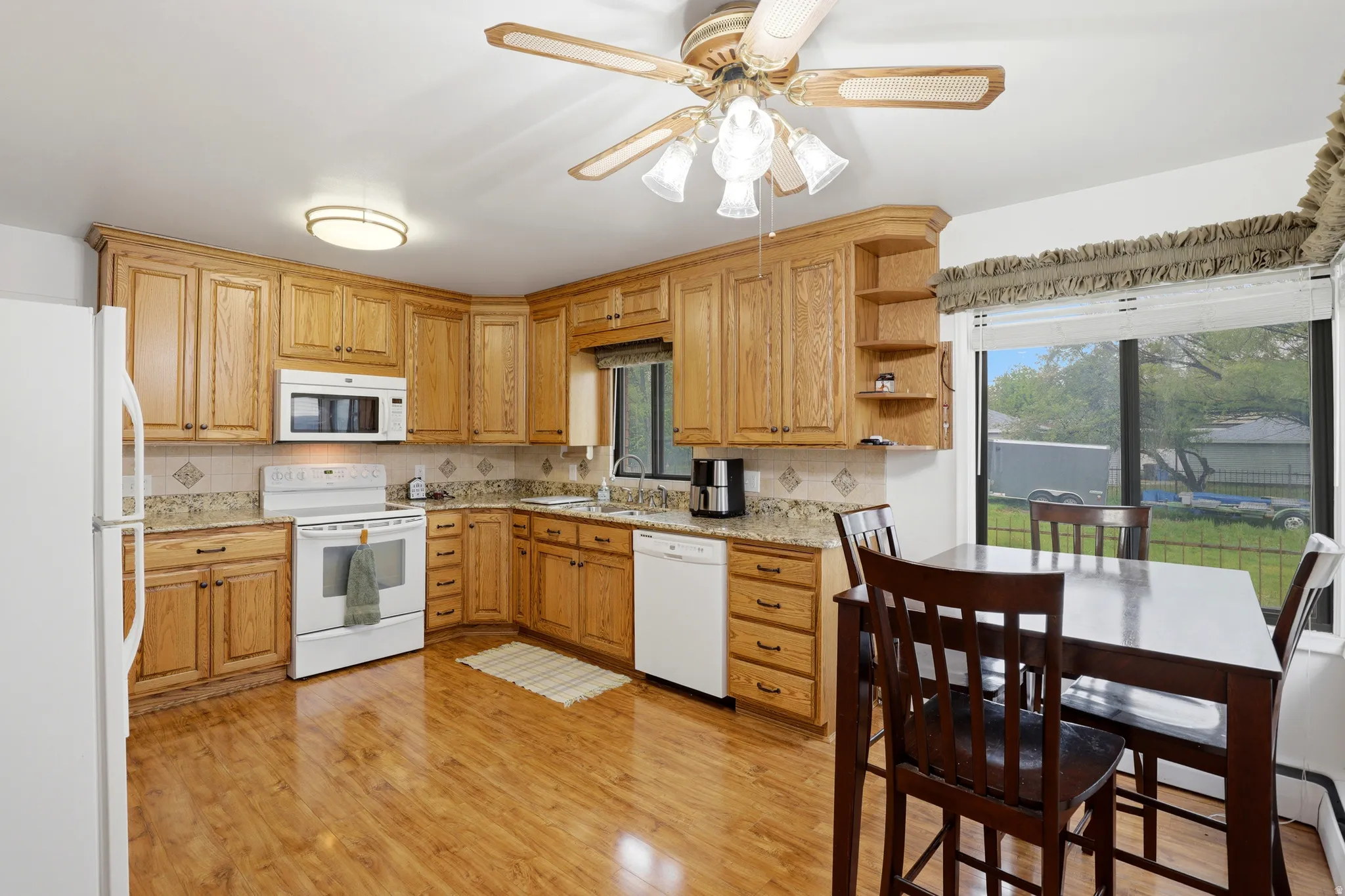 Kitchen with white appliances, light wood-type flooring, a ceiling fan, open shelves, and light stone counters