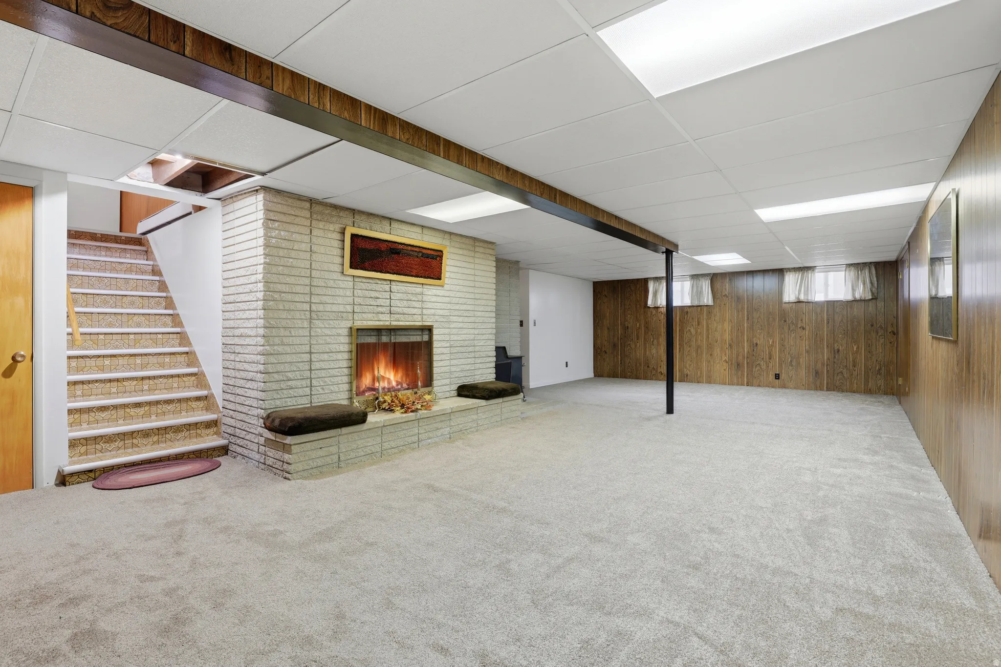 Basement featuring a paneled ceiling, a brick fireplace, carpet flooring, and wood walls