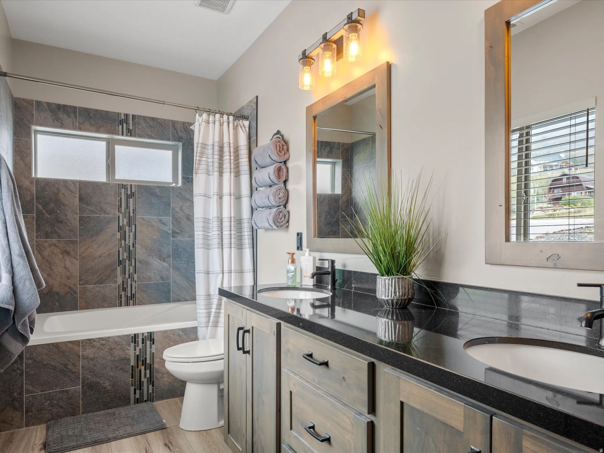 Full bath with double vanity, tiled shower / bath combo, and light wood-style flooring